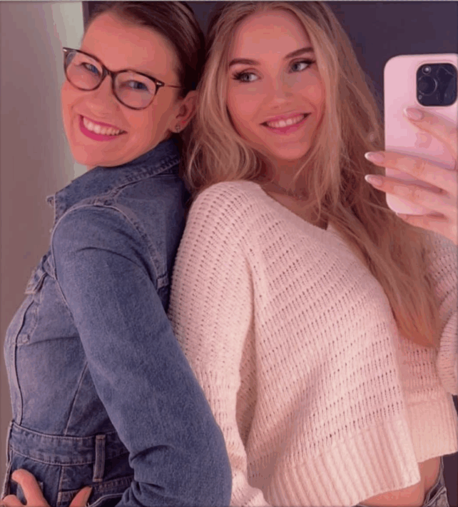 Das Team von Jeans4ALL: Zwei Frauen, Mutter und Tochter, stehen lächelnd Rücken an Rücken. Die eine trägt eine Brille und eine Jeansjacke, während die andere, die das Selfie macht, lange blonde Haare hat und einen weißen Strickpullover trägt.