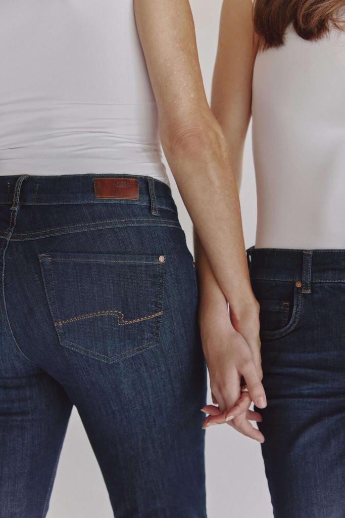 zwei personen in dunkelblauen jeans und weißen oberteilen stehen seite an seite und halten sich an den händen. das bild ist so beschnitten, dass ihre oberkörper und beine von der taille abwärts zu sehen sind.